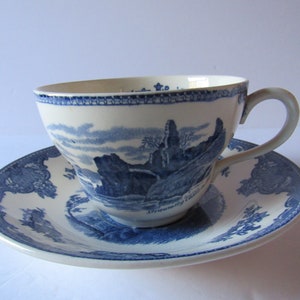 May include: A blue and white porcelain teacup and saucer set with a scenic landscape design. The saucer features a blue and white floral border. The teacup has a blue and white landscape scene with the text "Stranraer Castle" on the bottom.