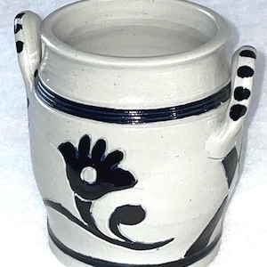 May include: A white ceramic jar with two handles and blue and black floral designs. The jar has a wide mouth and is perfect for storing small items.