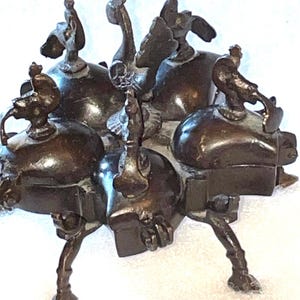 May include: A bronze sculpture featuring multiple bulbous forms, each topped with a stylized bird or creature. The sculpture has a dark, aged patina and is supported by three legs. The overall design is intricate and abstract.