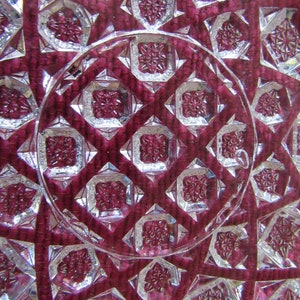 K&ouml;nnte beinhalten: Nahaufnahme einer durchsichtigen Glasschale mit einem geschliffenen Glasmuster. Die Schale hat eine tiefrote Farbe und ein geometrisches Design.