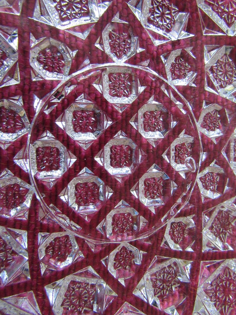 K&ouml;nnte beinhalten: Nahaufnahme einer durchsichtigen Glasschale mit einem geschliffenen Glasmuster. Die Schale hat eine tiefrote Farbe und ein geometrisches Design.