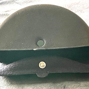 Op de afbeelding: Een donker olijfgroene, halfronde brillenkoker met een zwart, met vilt gevoerd interieur. De koker heeft een druksluiting en een klein, rond gat aan de bovenkant. De koker is ontworpen om brillen te beschermen.