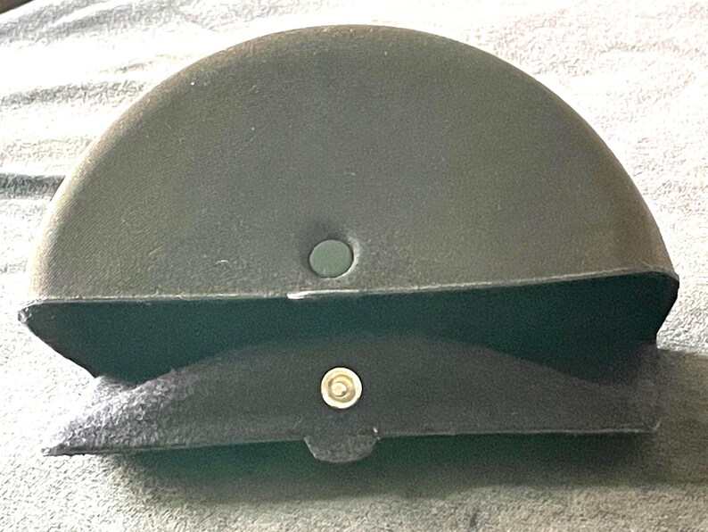 Op de afbeelding: Een donker olijfgroene, halfronde brillenkoker met een zwart, met vilt gevoerd interieur. De koker heeft een druksluiting en een klein, rond gat aan de bovenkant. De koker is ontworpen om brillen te beschermen.