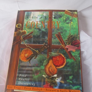 May include: A book titled "Glorious Country" with a window scene on the cover. The window is decorated with dried fruit, cinnamon sticks, and other natural elements. The book features food, crafts, and decorating ideas.