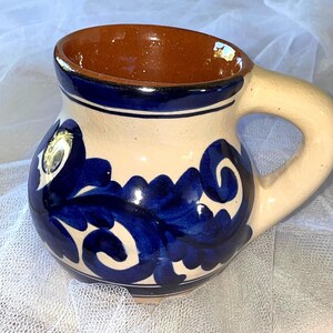 May include: A ceramic mug with a blue and white floral design. The mug has a brown clay interior and a handle.