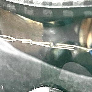 Op de afbeelding: Een zilveren metalen auto-embleem met de letters "D" en "A" zichtbaar. Het embleem is bevestigd op een donkere ondergrond, mogelijk de buitenkant van een auto. De afbeelding is een close-up.