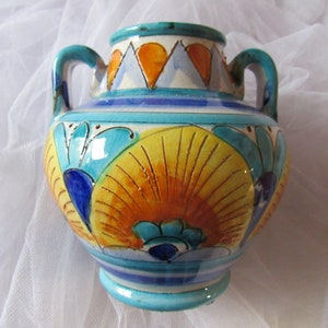 May include: A small, hand-painted ceramic vase with two handles. The vase is decorated with a colorful floral pattern in shades of blue, yellow, orange, and white.