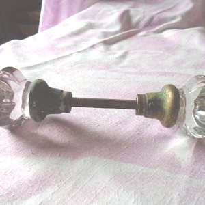 May include: A pair of clear glass door knobs with a metal connecting rod. The knobs have a faceted design.