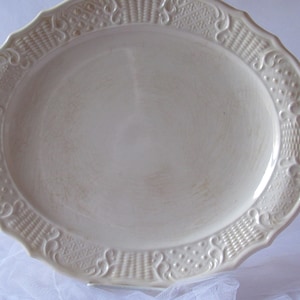 May include: A white oval serving platter with a raised, embossed design around the edge. The design features a repeating pattern of woven baskets and floral motifs.