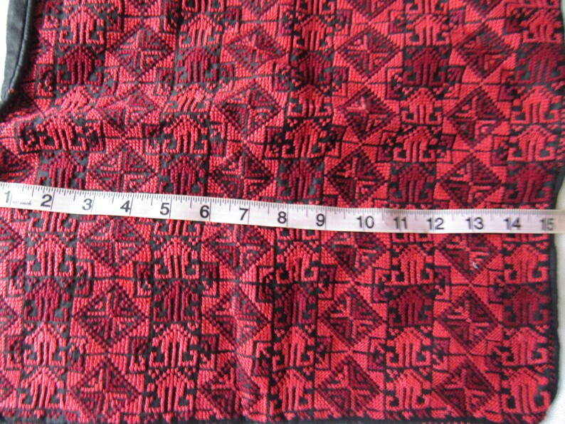 Może przedstawiać: Czerwony materiał z czarnym geometrycznym wzorem. Taśma miernicza umieszczona na materiale, pokazuje pomiar 38 cm.
