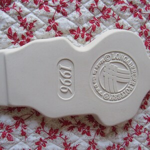 Puede incluir: Adorno de cer&aacute;mica blanca con forma de persona con un c&iacute;rculo en relieve en la parte posterior que dice "Longaberger Pottery" y "1996" en la parte delantera.
