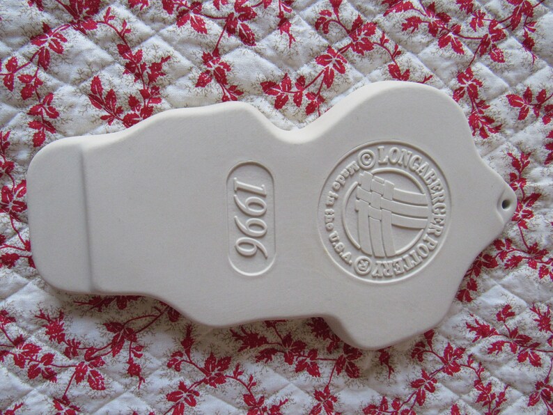 Puede incluir: Adorno de cer&aacute;mica blanca con forma de persona con un c&iacute;rculo en relieve en la parte posterior que dice "Longaberger Pottery" y "1996" en la parte delantera.