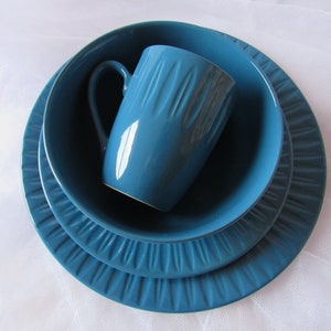 May include: A set of three blue ceramic plates and a matching blue ceramic mug. The plates have a textured, rippled design.