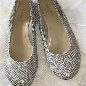 May include: A pair of gray snake-skin patterned ballet flats with the brand name "Vionic" printed on the inside of each shoe.