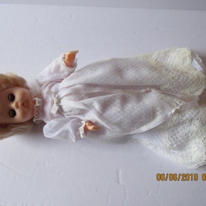 May include: A white doll with blonde hair wearing a white lace dress.