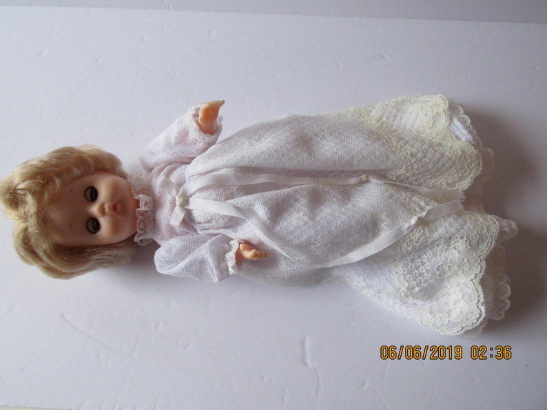 May include: A white doll with blonde hair wearing a white lace dress.