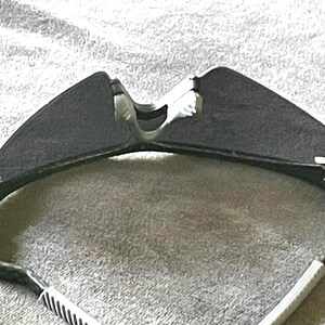 Op de afbeelding: Sportzonnebril met een donkergrijze lens en een zwart-wit montuur. De zonnebril heeft een strak, modern design, met een gebogen vorm en een comfortabele pasvorm. De pootjes van de zonnebril zijn wit met zwarte strepen.