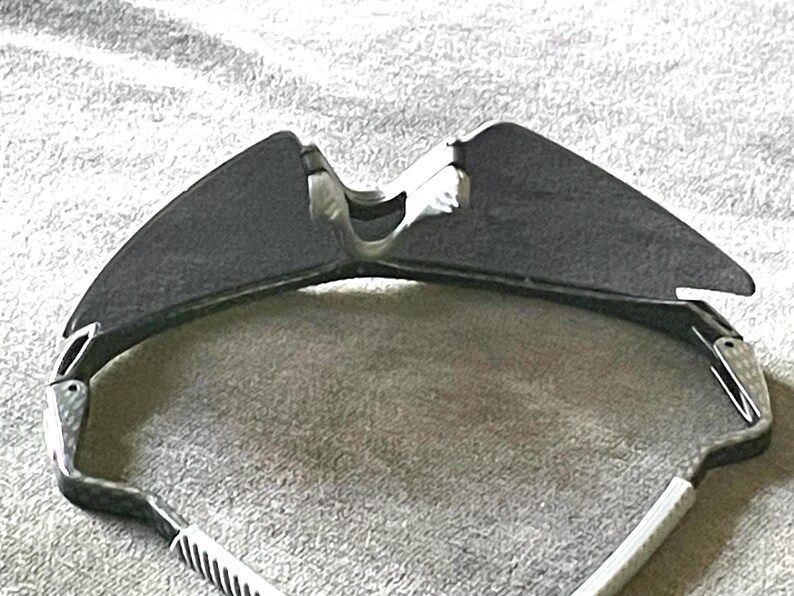 Op de afbeelding: Sportzonnebril met een donkergrijze lens en een zwart-wit montuur. De zonnebril heeft een strak, modern design, met een gebogen vorm en een comfortabele pasvorm. De pootjes van de zonnebril zijn wit met zwarte strepen.