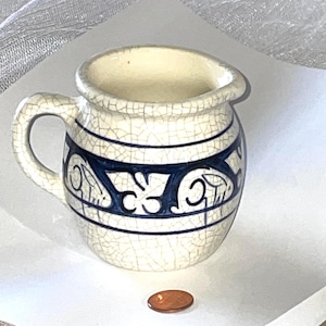 May include: A small white ceramic pitcher with a blue and white floral design. The pitcher has a crackled glaze and a handle.