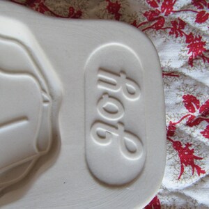Puede incluir: Plato para hornear de cer&aacute;mica blanca con una forma ovalada en relieve y la palabra "Pop" grabada en el lateral.