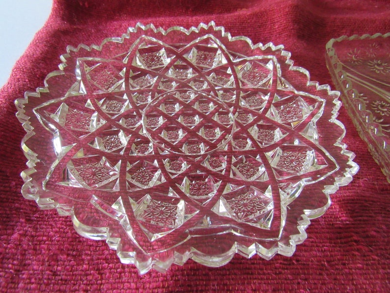 K&ouml;nnte beinhalten: Ein klarer Glasteller mit einem gewellten Rand und einem geometrischen Muster. Der Teller ist aus geschnittenem Glas und hat ein Sternmuster.