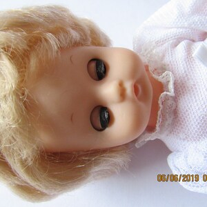 May include: A close-up of a porcelain doll with blonde hair and closed eyes. The doll is wearing a white lace dress with a bow.