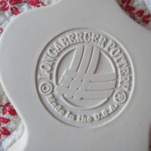 Puede incluir: Un plato de cer&aacute;mica blanco con un logotipo en relieve que dice "Longaberger Pottery" y "Made in the U.S.A."