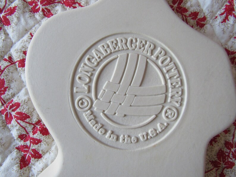 Puede incluir: Un plato de cer&aacute;mica blanco con un logotipo en relieve que dice "Longaberger Pottery" y "Made in the U.S.A."