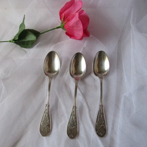 May include: Three silver spoons with ornate designs on the handles. The spoons are arranged in a row on a white background.