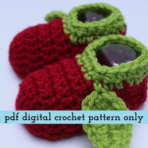 K&ouml;nnte beinhalten: Ein Paar handgefertigte Baby-H&auml;kel-Schuhe in leuchtendem Rot, mit gr&uuml;nen Verzierungen und Bl&auml;ttern. Die Schuhe haben ein einzigartiges Design und sind perfekt f&uuml;r Neugeborene. Der Text "pdf digital crochet pattern only" ist zu sehen.