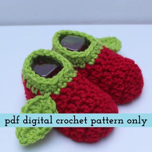 K&ouml;nnte beinhalten: Handgefertigte Baby-H&auml;kel-Schuhe in Erdbeerform. Die Schuhe sind rot mit gr&uuml;nen Verzierungen und Bl&auml;ttern. Der Text "pdf digital crochet pattern only" ist auf einem hellblauen Banner zu sehen.