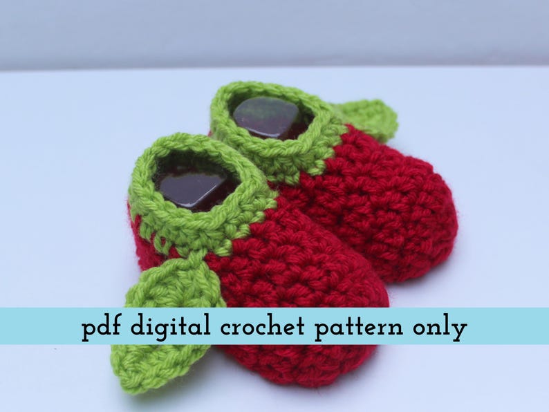 K&ouml;nnte beinhalten: Handgefertigte Baby-H&auml;kel-Schuhe in Erdbeerform. Die Schuhe sind rot mit gr&uuml;nen Verzierungen und Bl&auml;ttern. Der Text "pdf digital crochet pattern only" ist auf einem hellblauen Banner zu sehen.