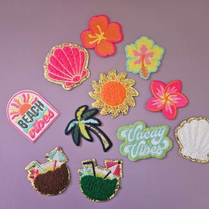 May include: A collection of eleven embroidered patches featuring tropical themes including a pink seashell, orange and yellow hibiscus flowers, a sun, a palm tree, a white seashell, and two coconut drinks. Text reads Beach Vibes and Vacay Vibes.