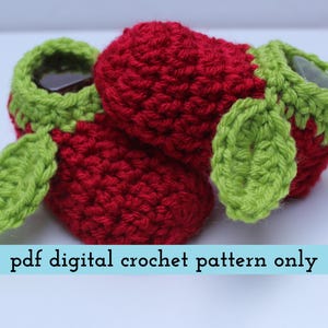 K&ouml;nnte beinhalten: Geh&auml;kelte Babyschuhe in Form von Erdbeeren. Die Schuhe sind rot mit gr&uuml;nen Verzierungen und Bl&auml;ttern. Der Text "pdf digital crochet pattern only" wird auf hellblauem Hintergrund angezeigt.