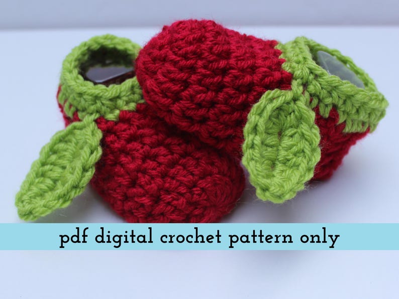 K&ouml;nnte beinhalten: Geh&auml;kelte Babyschuhe in Form von Erdbeeren. Die Schuhe sind rot mit gr&uuml;nen Verzierungen und Bl&auml;ttern. Der Text "pdf digital crochet pattern only" wird auf hellblauem Hintergrund angezeigt.