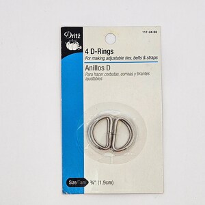 May include: A package of four silver-colored metal D-rings by Dritz, labeled for making adjustable ties, belts, and straps. The packaging includes the text 4 D-Rings, Anillos D, and a size specification of 3/4 inch (1.9 cm) printed on the card.