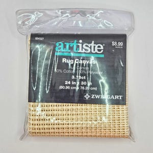 May include: A beige rug canvas in a clear plastic package with a black label reading Artiste Rug Canvas, 50% Cotton 50% Polyester, 3.75ct, 24 in x 30 in (60.96 cm x 76.20 cm), and Zweigart. The grid-like fabric is visible through the bottom of the bag.