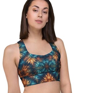 Op de afbeelding: Sportbeha met een kleurrijk, abstract patroon in tinten teal, oranje en marineblauw. De beha heeft een ronde halslijn en een racerback-ontwerp. Het model draagt ​​een zwarte legging.
