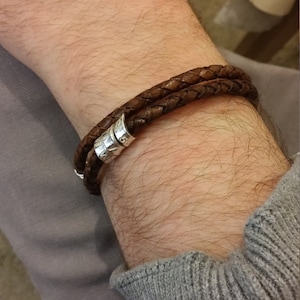 May include: A brown leather bracelet with silver metal accents. The bracelet is braided and has a simple design.