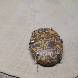 May include: A silver chain necklace with a brown and gold oval pendant. The pendant has a unique marbled pattern and is set in a silver bezel.