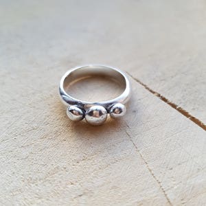 May include: A silver ring with three round, textured bumps on the band.