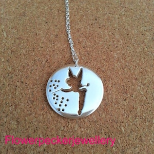 May include: Silver necklace with a round pendant featuring a cutout silhouette of a fairy with wings spread, holding a flower. The pendant has a dotted design around the edge.