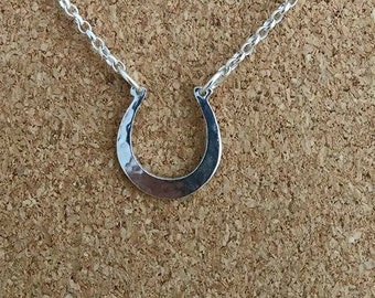 May include: A silver horseshoe pendant necklace on a silver chain. The horseshoe is hammered and has a smooth, polished finish.