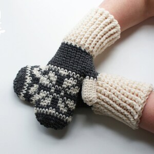 May include: A pair of crocheted mittens with a white and gray snowflake pattern. The mittens are made with a chunky yarn and have a ribbed cuff.