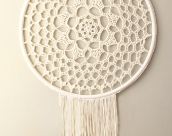 May include: A white crocheted dream catcher with a circular hoop and long fringe hanging from the bottom.