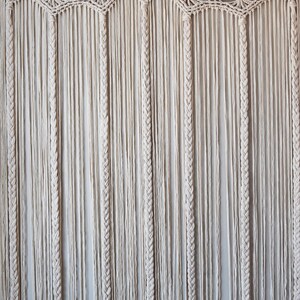 May include: A white macrame wall hanging with a scalloped top and long strands of knotted cord.