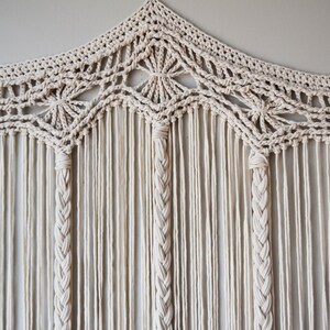 May include: A white macrame wall hanging with a geometric design and a fringe border.