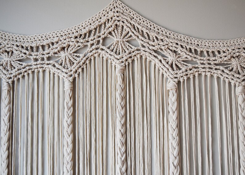 May include: A white macrame wall hanging with a geometric design and a fringe border.