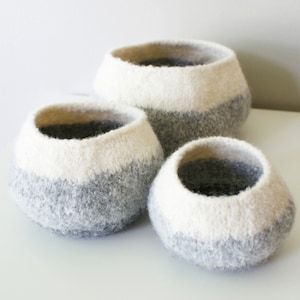 May include: Three gray and white felted wool baskets of different sizes. The baskets are round and have a white top and a gray bottom.