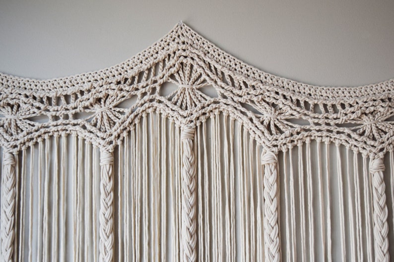 May include: A white macrame wall hanging with a geometric design and fringe. The hanging is made of cotton cord and has a bohemian style.